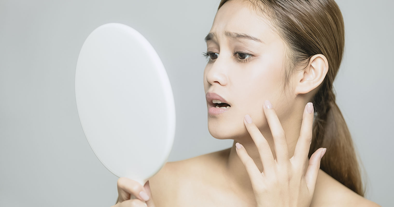 Woman looking into a mirror worried about her skin condition