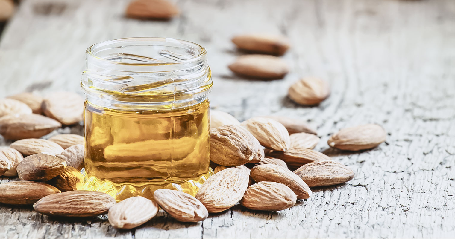 Sweet Almond Oil, first extraction, in a small glass jar, dry almond nuts on an old wooden background