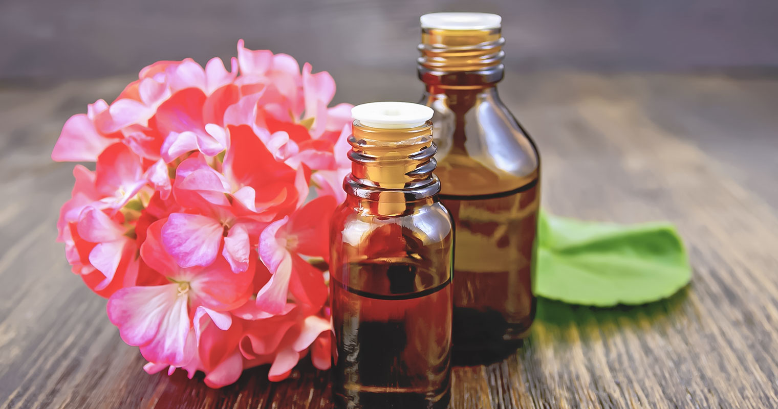2 bottles of Geranium oil in front of Geranium flower on a table