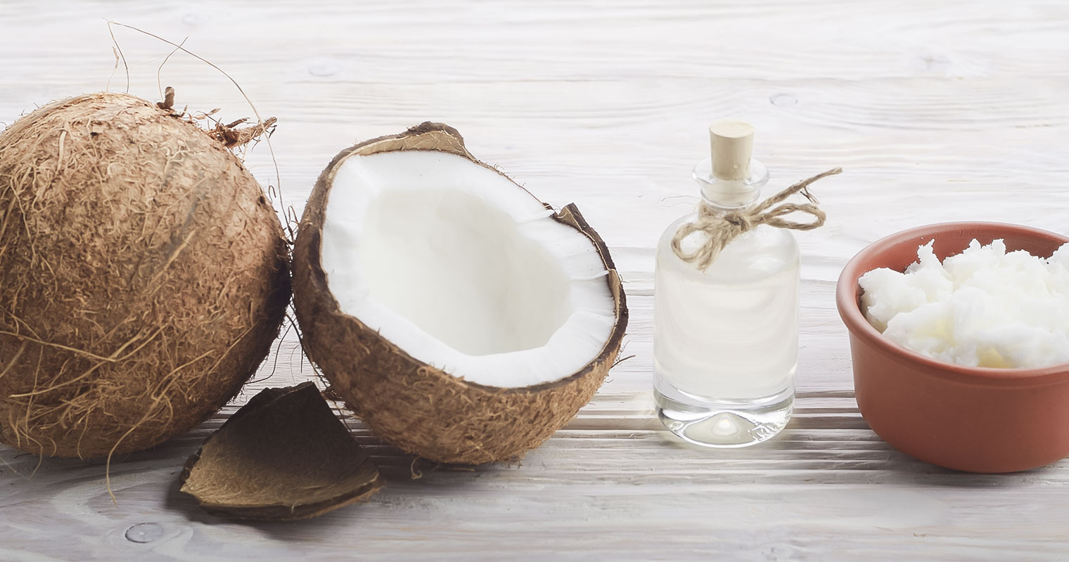 An opened coconut with a bottle of coconut oil and a bowl of coconut meat