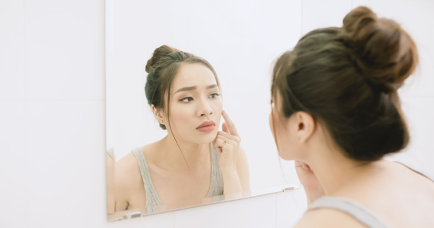 young woman looking to mirror at home bathroom looking worried